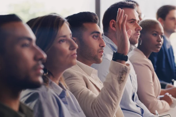 Group of people sitting in a row with one man raising his hand.
