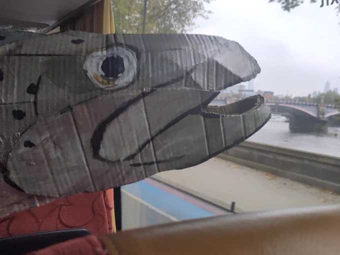 Cardboard model of a salmon looks out of a coach window at the river Thames