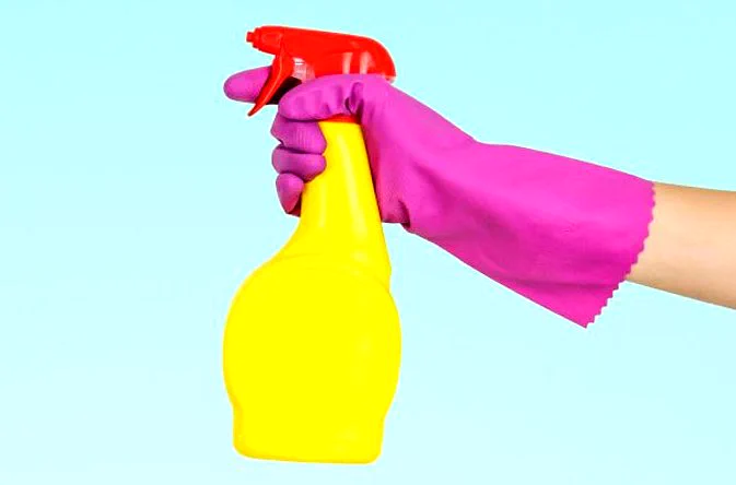 Image shows pink rubber gloved hand holding yellow spray bottle