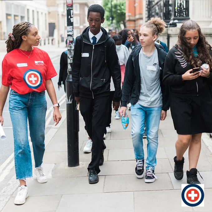 A student and three prospective students walking on a city street on a tour of UCL. They seem engaged in casual conversation.