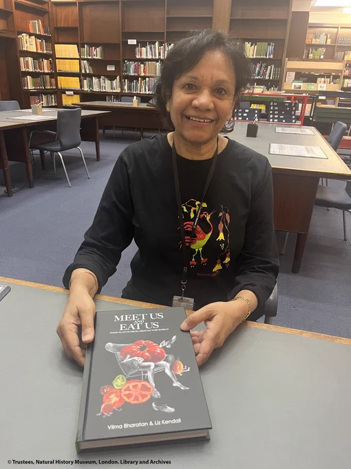 Person sitting at a library desk facing the camera, holding their book.