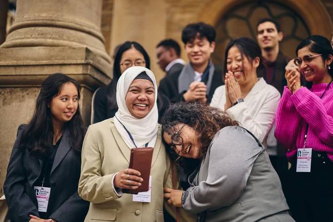 A group of Equitech Futures Fellows smile and hug on the steps of Rhodes House