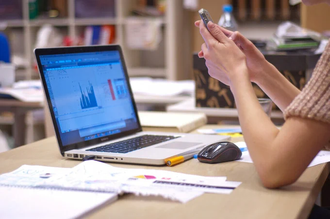 College student holding their phone with their computer open while they study.