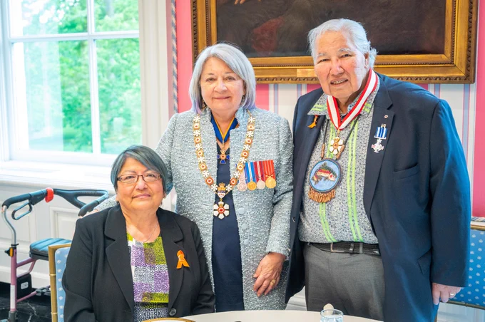 Governor General Mary Simon is standing between a woman and a man. The woman is seated.