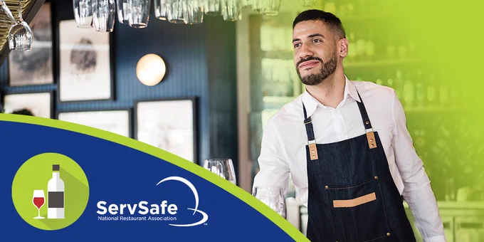 Smiling server in an apron standing in a bar, with the ServSafe logo of the National Restaurant Association visible.