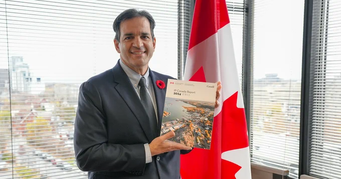 Picture of CIPO CEO, Konstantinos Georgaras, holding a copy of the IP Canada Report 2024, beside the Canadian flag.