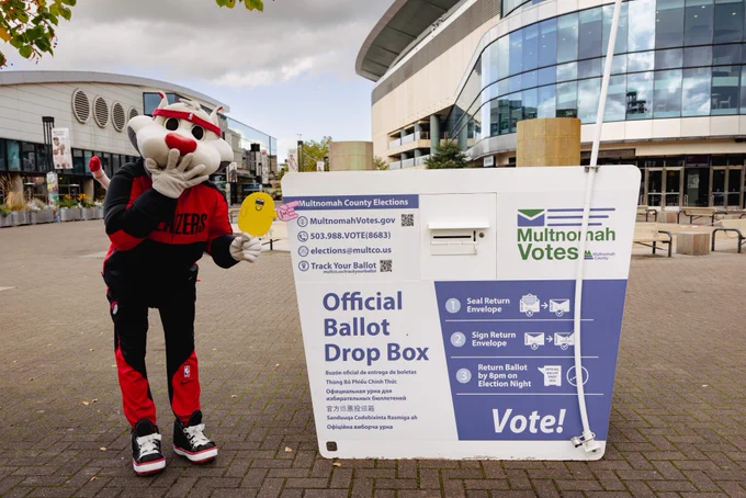 Blaze the Trail Cat at the Moda Center next to the Multnomah County Official Drop Box holding Blobby. 
