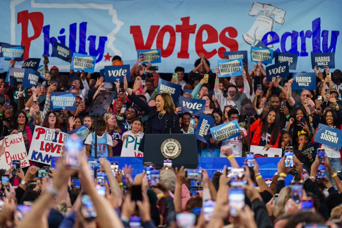 An image of Vice President Kamala Harris at a campaign event in Philadelphia, Pennsylvania. Behind Vice President Harris is an audience holding various signs that read, "Vote," "Harris Walz," and "Pennsylvania Votes Early."