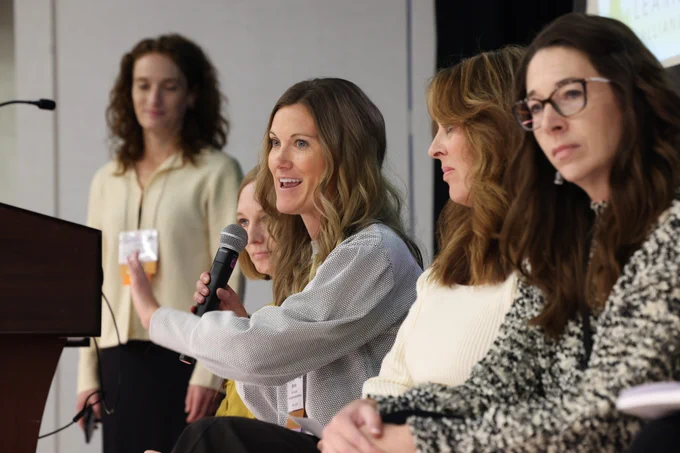 Five participants, one speaking into a microphone, at QM Connect 2024.
