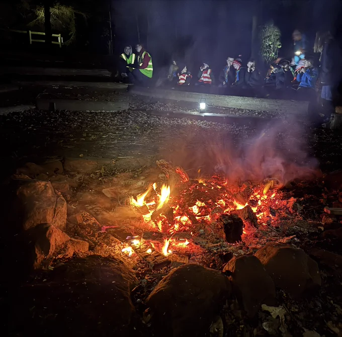 Campfire with Squirrel and Beaver Scouts behind, two young leaders are also present.