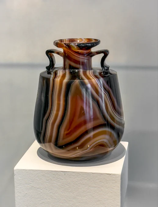 Small amphoriskos perfume bottle, made of banded agate. The shape is like a fat amphora (hence the name - ‘small amphora’) with a round flat bottom; two tiny handles support the neck, which flares out at the top, where the opening would have once had a stopper. The banded agate has stripes of black, white, cream, red, orange, and yellow. Spectacular.

In Hellenistic and Roman times, vessels made in semiprecious stone were much sought after as symbols of wealth and sophistication. They were used as diplomatic gifts or treasured as heirlooms, and many of them found their way into royal tombs or imperial collections, both in antiquity and later. Their rarity also encouraged imitations in both glass and pottery.

Roman, late 1st century BCE–early 1st century CE. 

Met Museum, New York (2001.253))