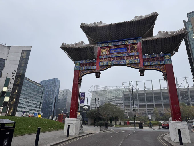 A large Chinese  (I believe) style gate. With large buildings including a football stadium visible behind.