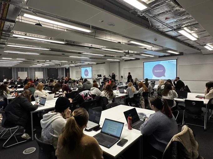 A room of seated students facing speakers