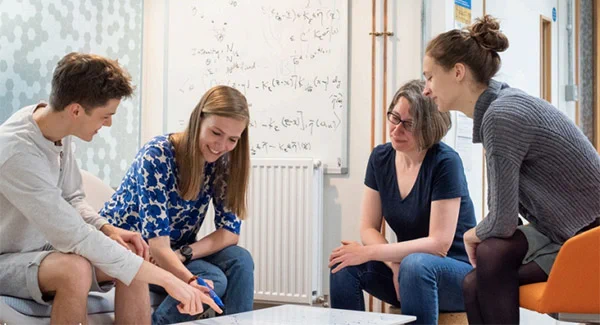 Students discussing a equation written on to a white desk.  Credit: John Cairns