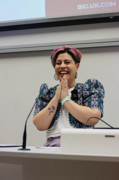 Sarah smiles widely whilst presenting from a lectern