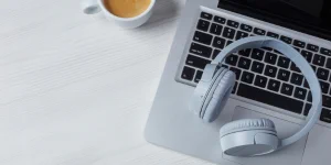 Image of laptop with headphones sitting on keyboard.  Cup of coffee beside laptop.