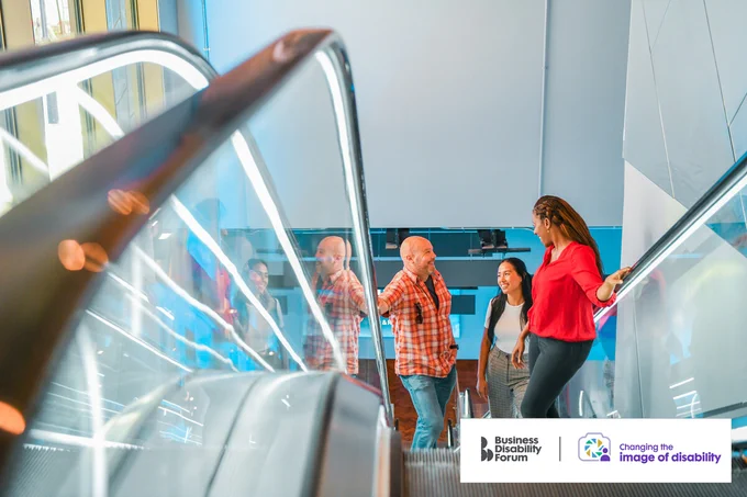 Group of 3 friends chat on an escalator. The 2 people on the left have less-visible disabilities. The Business Disability Forum 'Changing the image of disability' logo is in the lower right corner of the image.