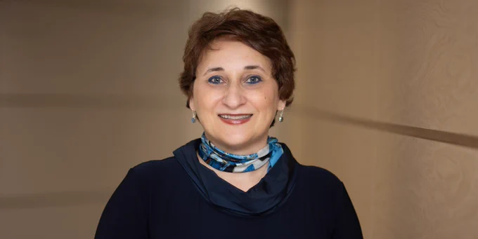 Smiling, Dr. Octavia Dobre is seen wearing a dark-colour dress, blue and silver colour earrings and multi-colour scarf.