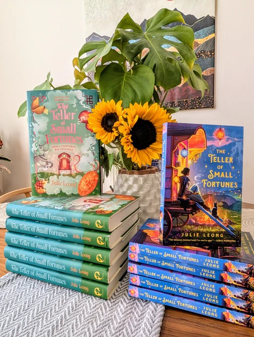 stacks of both US and UK editions of The Teller of Small Fortunes in front of a vase of sunflowers