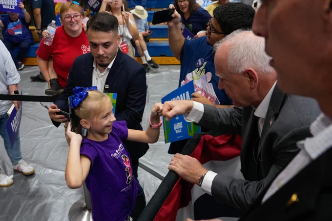 Governor Tim Walz fist bumps a young supporter at an event.