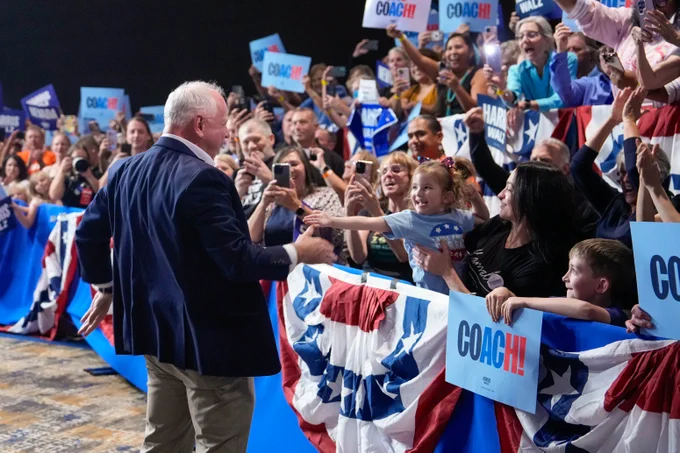 Governor Tim Walz talks to a young child in a crowd of supporters.