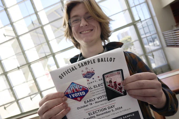 Person smiling and holding an “Official Sample Ballot” with “I Voted” stickers.
