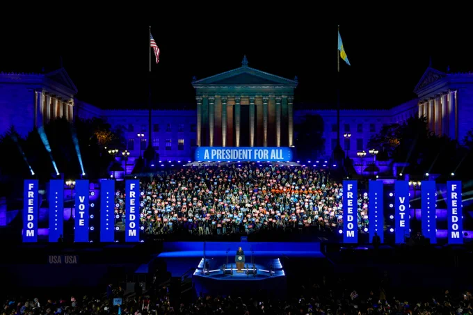 Night view of a large crowd at a political rally in front of the Philadelphia Museum of Art, prominently featuring the phrase 'A President for All' above the stage, flanked by American flags and banners with the words 'FREEDOM' and 'VOTE.'