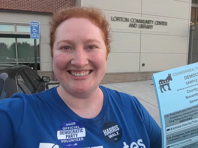 Me in front of the Lorton Community Center with a stack of democratic sample ballots and a Harris/Walz sticker and Official Democratic Party Volunteer sticker and blue AFT Votes shirt.