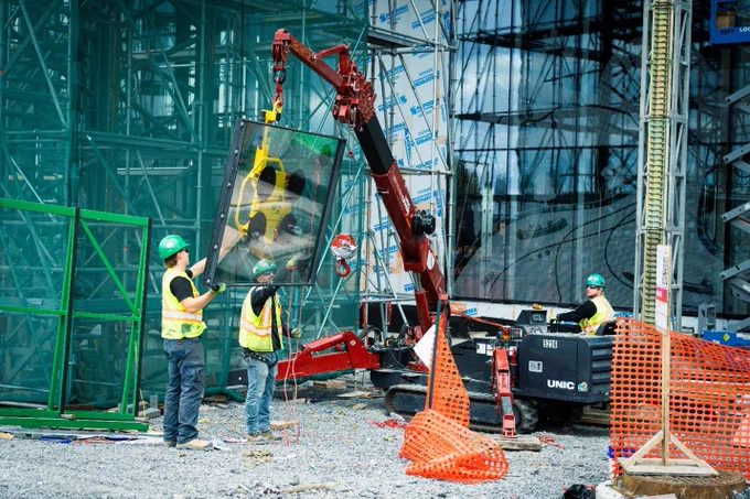 Deux ouvriers aident à soutenir une fenêtre de l’auditorium pendant qu’un autre ouvrier utilise une machine. 