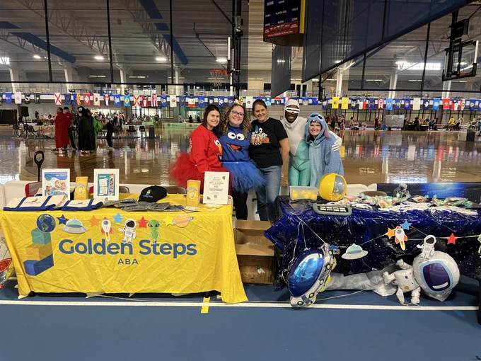 Golden Steps staff posed together behind their candy booths. 4 of the five people in the picture are dressed up in kid-friendly costumes. 