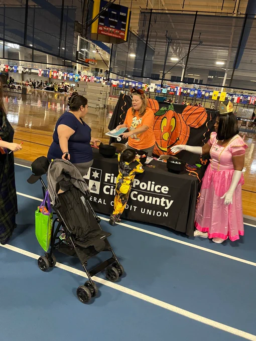 Two people dressed in halloween costumes handing out candy behind a table with a Fire Police City county Federal Credit Union table cloth. 