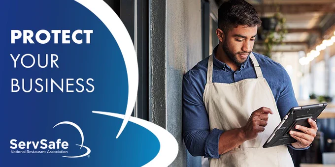 An individual in an apron using a tablet next to a 'Protect Your Business' sign with the ServSafe and National Restaurant Association logos.