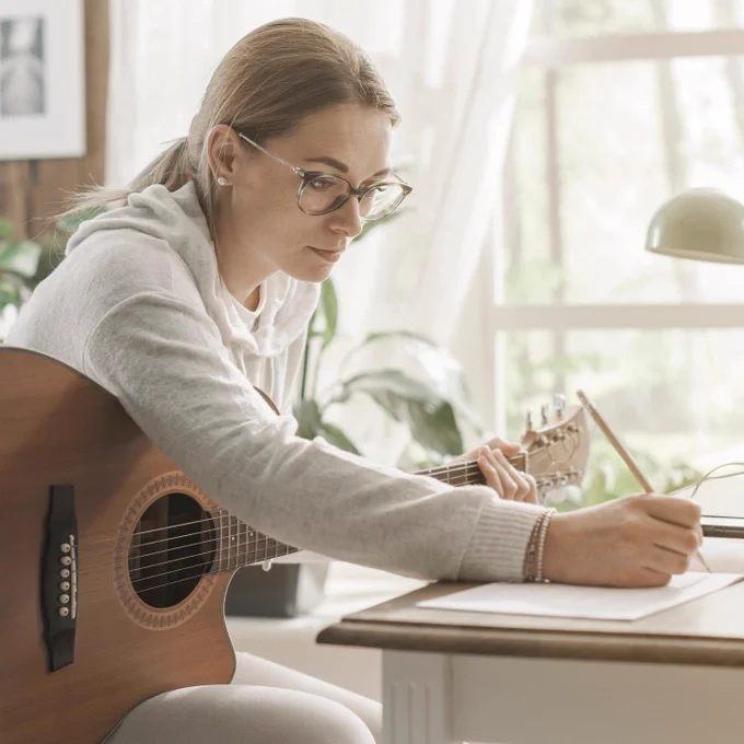 Photo of a girl with a guitar sitting at a desk writing on a piece of paper