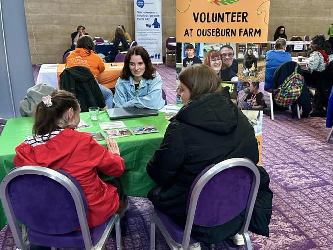 A representative from Ouseburn farm talking with two attendees at a table in the Banqueting Hall, Civic Centre.