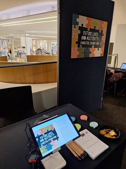 A picture of our sign, and a tablet on a table displaying the front image from the exhibition  
