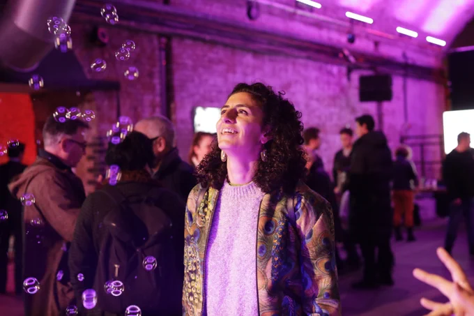 Person smiling joyfully at floating bubbles in a lively indoor event space.