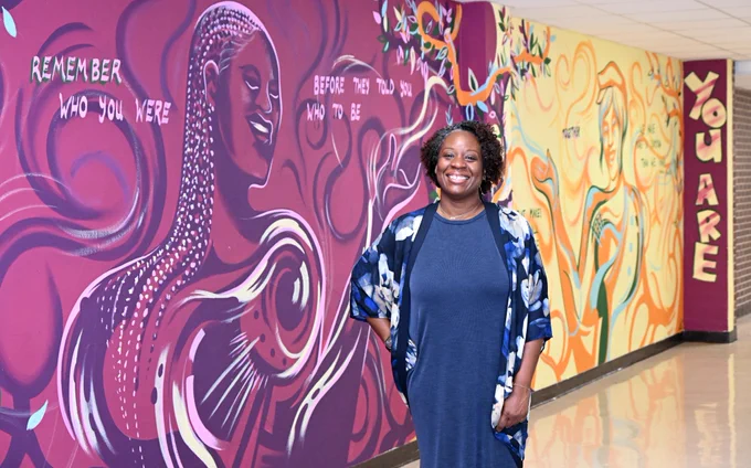 Librarian Quinntana Slaughter in front of a mural that says "Remember Who You Were Before They Told  You Who to Be."
