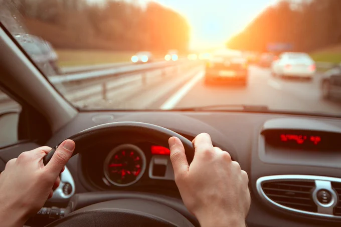 View from inside a car during a sunset drive, showing hands on the steering wheel and the highway ahead.