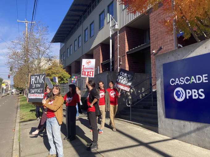People holding signs picket outside the Cascade PBS office.