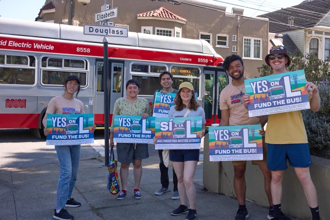6 volunteers holding Yes on L signs in front of a 35 Eureka Muni bus