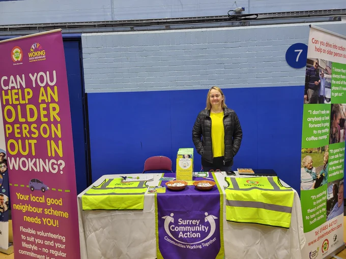 A volunteer stands behind a table with information about good neighbour schemes.