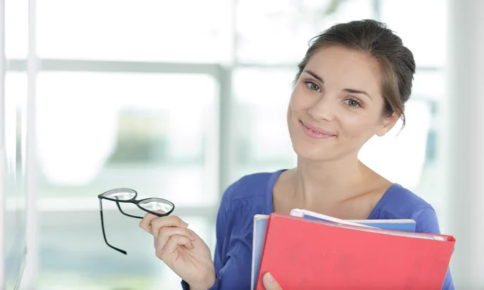 Stock image of receptionist at work, holding glasses and notebooks. 