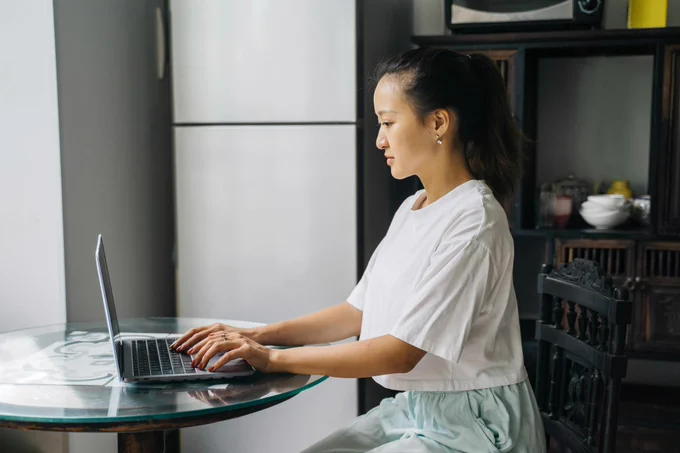 Young woman sitting at a kitchen table, using a laptop