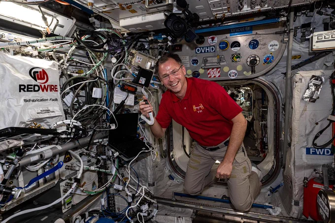
iss072e034816 (Oct. 11, 2024) -- NASA astronaut and Expedition 72 Flight Engineer Nick Hague is photographed during an ISS Ham Radio session. He is facing the camera and holding the radio microphone to talk with students on Earth. Hague is wearing a red polo and khakis.