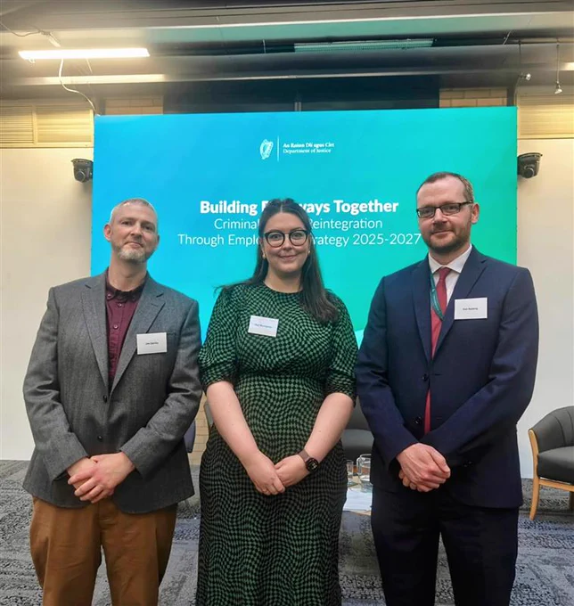 Image of three people in a row standing facing the camera in front of a screen reading 'building pathways together.