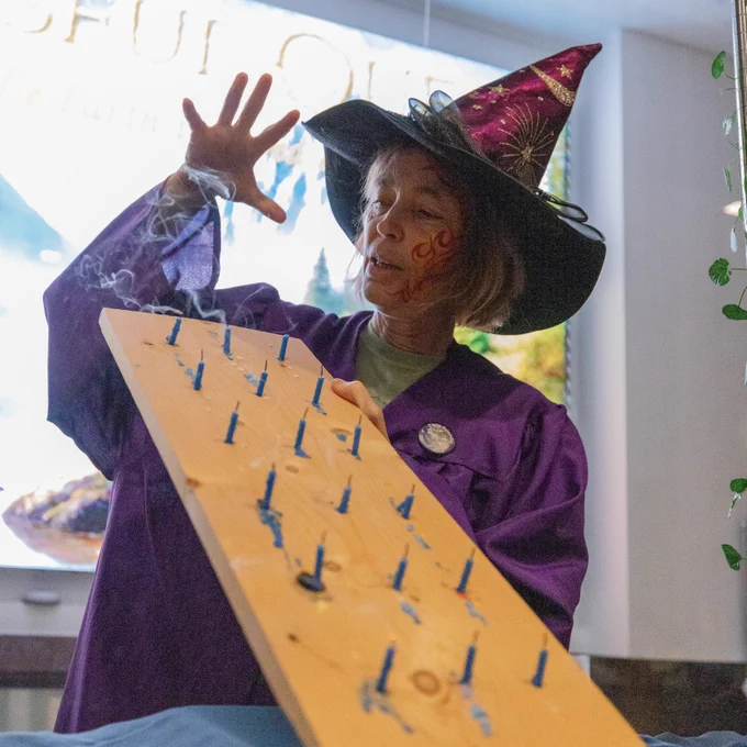 An NSF NCAR Wizard in a purple robe and wizard hat holding her hand above a wooden board covered in candles. 