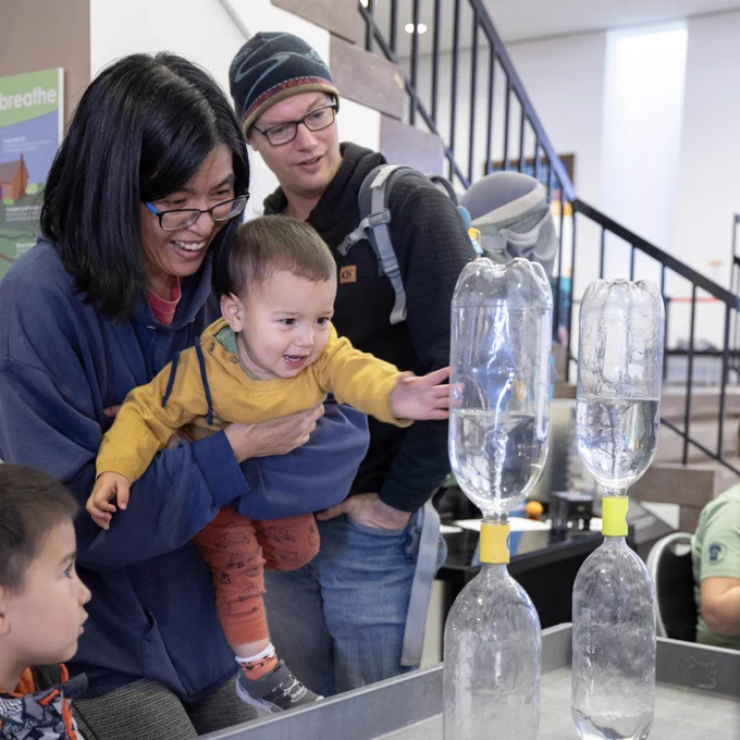 A family smiling curiously at a tornado in a bottle. 