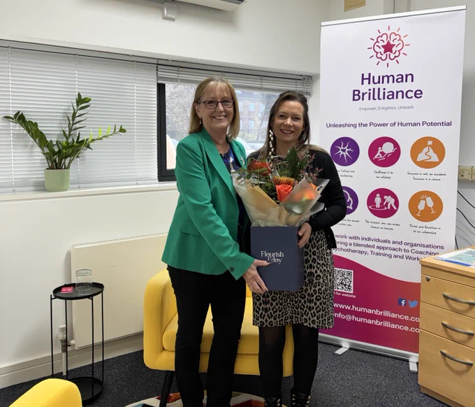 Freya Cross and Gemma Wardell stood together smiling as Freya hands Gemma a box of flowers in Gemma's office.