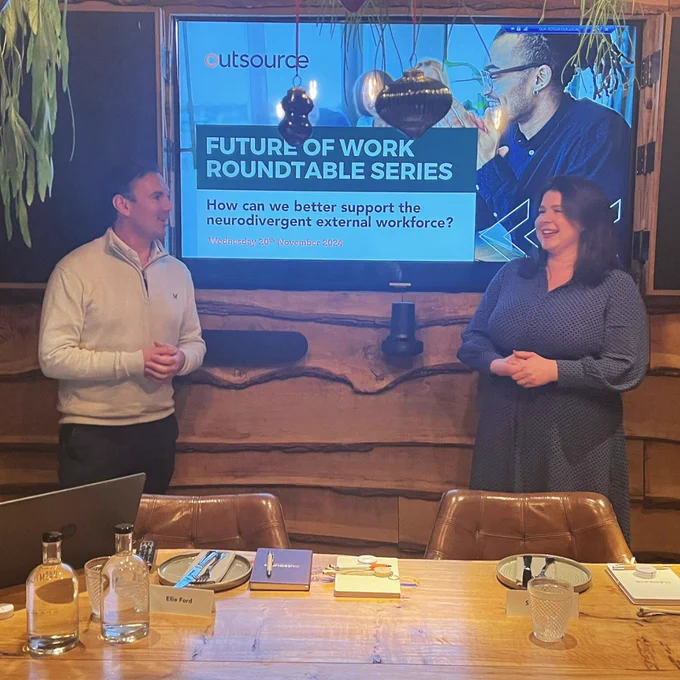 Two people stood in front of a screen talking in the venue and smiling.