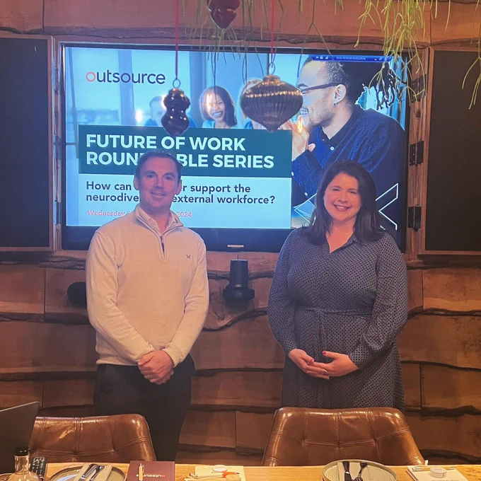 Two people stood in front of a screen smiling.